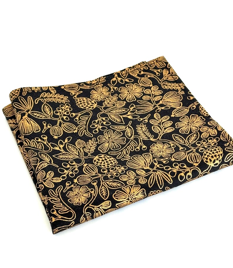 Puede incluir: Un pa&ntilde;uelo de bolsillo negro con un patr&oacute;n floral dorado. El patr&oacute;n presenta hojas, flores y bayas.