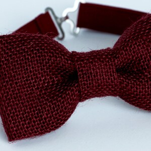 May include: A burgundy bow tie made of burlap fabric. The bow tie is tied with a simple knot and has a plain design.