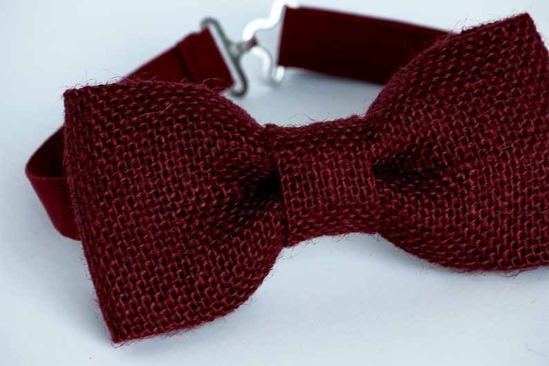 May include: A burgundy bow tie made of burlap fabric. The bow tie is tied with a simple knot and has a plain design.