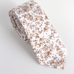 May include: A white tie with a brown floral pattern. The tie is rolled up and the pattern is visible.