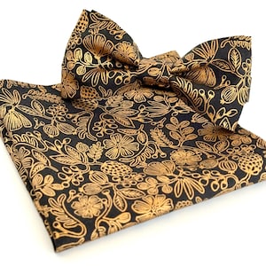 Puede incluir: Una pajarita y un pa&ntilde;uelo de bolsillo negros con un patr&oacute;n floral dorado.