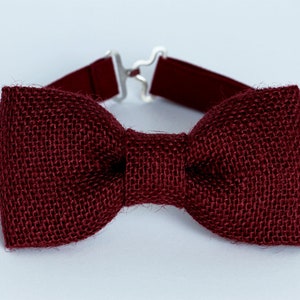 May include: A burgundy bow tie made of burlap fabric. The bow tie has an adjustable strap.