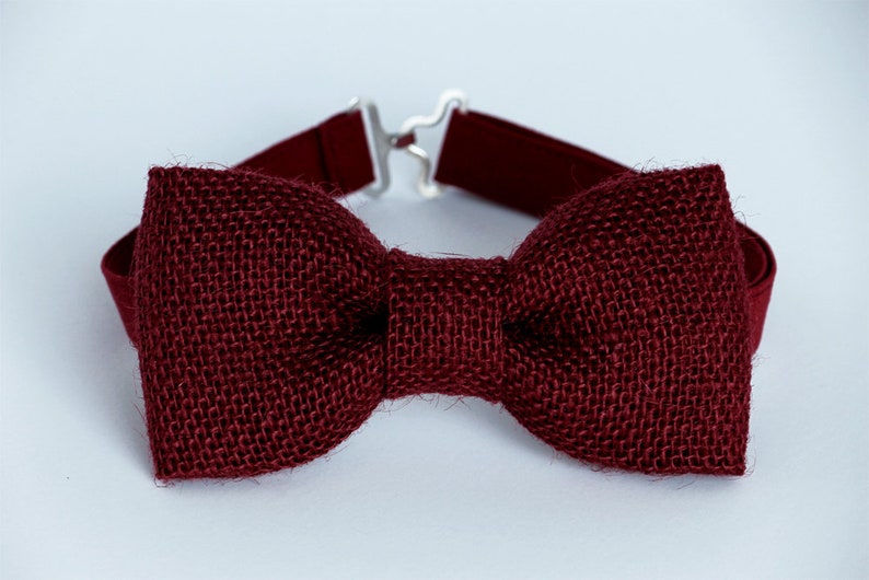 May include: A burgundy bow tie made of burlap fabric. The bow tie has an adjustable strap.
