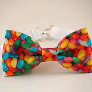 May include: A bow tie with a colorful jelly bean pattern. The bow tie is made of fabric and has a white adjustable strap.