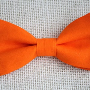 May include: A bright orange bow tie made of fabric. The bow tie is tied and ready to wear.