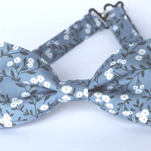 May include: A blue bow tie with a white floral pattern. The bow tie has a black adjustable strap.