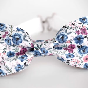 May include: A white bow tie with a floral pattern featuring blue, pink, and green flowers.