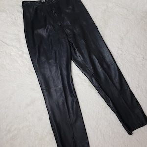 Könnte beinhalten: Schwarze Lederhose mit hoher Taille und Knopfleiste. Die Hose hat eine schmale Passform und ist aus weichem, geschmeidigem Leder gefertigt. Der Markenname "MIXIE" ist auf dem Bund sichtbar.