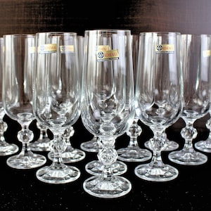 Puede incluir: Un juego de 10 copas de champán de cristal transparente con un tallo decorativo. Las copas están todas en fila sobre una superficie oscura. Cada copa tiene una etiqueta que dice "BOHEMIA CHECOSLOVAQUIA".