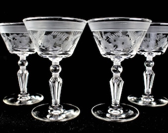 Op de afbeelding: Set van vier heldere glazen cocktailglazen met gegraveerde bloemenmotieven. De glazen hebben een brede kom en een hoge, slanke steel.