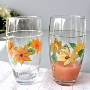 May include: Two clear glass tumblers with floral designs. The glass on the right contains a pink liquid.