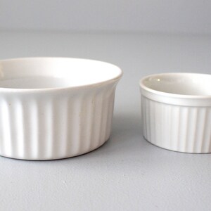 May include: Two white ceramic ramekins with vertical ribbed sides. One is larger than the other. The ramekins are on a light grey surface. The number "#3" is in the lower left corner.