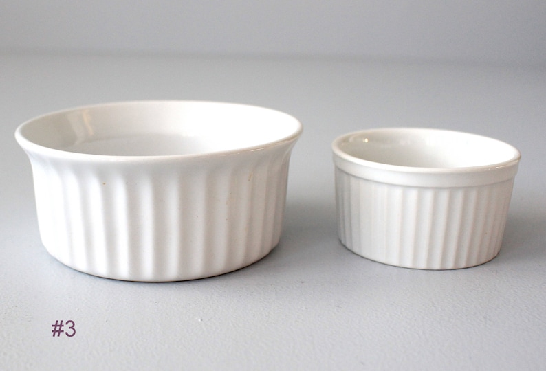May include: Two white ceramic ramekins with vertical ribbed sides. One is larger than the other. The ramekins are on a light grey surface. The number "#3" is in the lower left corner.