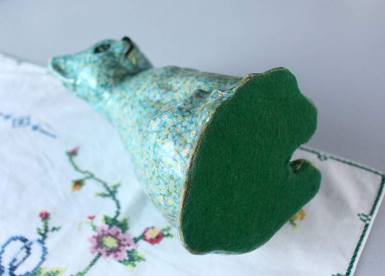 Pode incluir: Uma figura de gato de cer&acirc;mica azul com um fundo de feltro verde. O gato est&aacute; coberto com um padr&atilde;o floral de pequenas flores azuis.