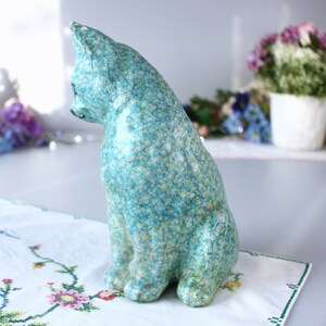 Pode incluir: Uma figura de cer&acirc;mica azul de um gato com um padr&atilde;o floral de miosotis. O gato est&aacute; sentado com a cabe&ccedil;a virada para o lado.