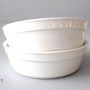May include: Two white ceramic bowls stacked. The bowls have a simple, rounded design with a slightly raised rim. The bowls are a creamy white colour and appear clean. The bowls are likely for serving or baking. Each bowl is approximately 15 cm in diameter.
