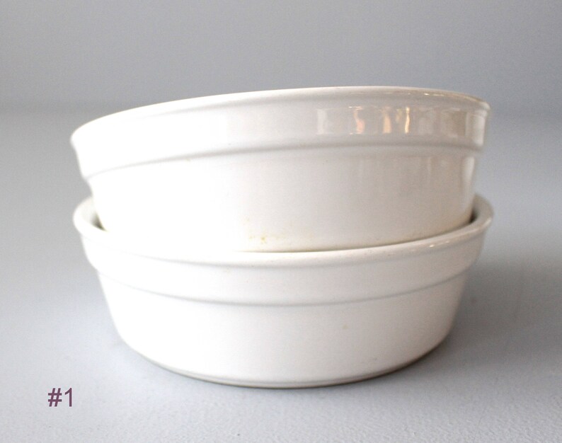 May include: Two white ceramic bowls stacked. The bowls have a simple, rounded design with a slightly raised rim. The bowls are a creamy white colour and appear clean. The bowls are likely for serving or baking. Each bowl is approximately 15 cm in diameter.
