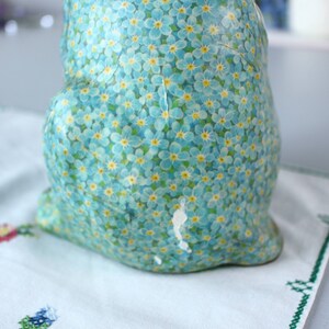 Pode incluir: Uma figurinha de cer&acirc;mica de um coelho coberta com um padr&atilde;o floral azul e amarelo. O coelho est&aacute; sentado em uma superf&iacute;cie branca.