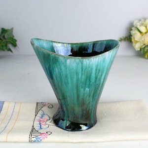 May include: A green and black glazed ceramic vase with a unique, wavy shape. The vase has a glossy finish and a light blue glaze in the centre.