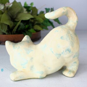 K&ouml;nnte beinhalten: Keramik-Katzenfigur in spielerischer Pose, bemalt in Cremegelb mit hellblauen floralen Akzenten. Die Katze ist gew&ouml;lbt, der Schwanz nach oben gebogen. Die Figur ist ein dekorativer Artikel.