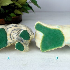 K&ouml;nnte beinhalten: Zwei Keramikfiguren, von unten betrachtet, mit gr&uuml;nen Filzbasen. Eine ist mit blauen Blumenmustern verziert, die andere mit einer hellblauen und gelben Oberfl&auml;che. Die Figuren sind mit A und B beschriftet.