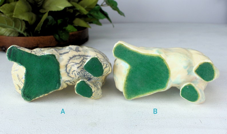 K&ouml;nnte beinhalten: Zwei Keramikfiguren, von unten betrachtet, mit gr&uuml;nen Filzbasen. Eine ist mit blauen Blumenmustern verziert, die andere mit einer hellblauen und gelben Oberfl&auml;che. Die Figuren sind mit A und B beschriftet.
