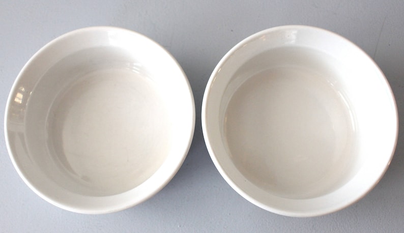 May include: Two white ceramic bowls with a simple, rounded design. The bowls are empty and have a smooth, glossy finish. The bowls are set against a light grey background. Ideal for serving soups, salads, or desserts.