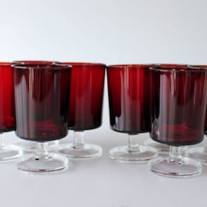 May include: Set of eight red glass wine glasses with clear stems and bases. The glasses are all the same size and shape.