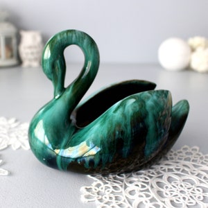 Puede incluir: Un macetero de cerámica en forma de cisne, esmaltado en verde con un efecto marmoleado. El cisne tiene un cuello largo y un cuerpo ancho con un centro hueco.