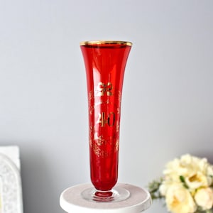 Peut inclure: Un vase en verre rouge avec un bord doré et un lettrage doré qui indique "CR 240".