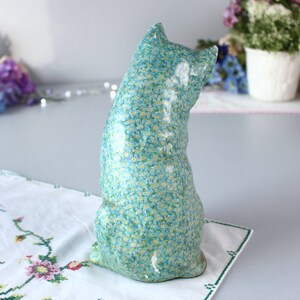 Pode incluir: Uma figura de cer&acirc;mica azul de um gato com um padr&atilde;o de flores de miosotis. O gato est&aacute; sentado com o rabo enrolado em torno do seu corpo.