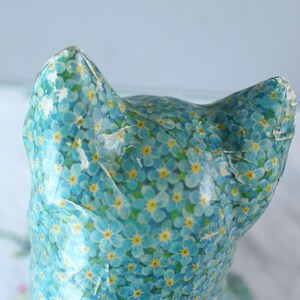 Pode incluir: Uma figura de cer&acirc;mica de um gato coberta com um padr&atilde;o floral azul e amarelo. O gato est&aacute; de costas para a c&acirc;mera e tem uma cauda longa.