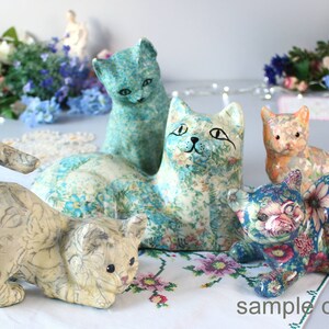 K&ouml;nnte beinhalten: Eine Sammlung dekorativer Katzenfiguren mit floralen Mustern in Blau, Creme und Orange. Die Katzen sind in verschiedenen Posen dargestellt. Der Satz "sample only" ist unten rechts sichtbar.