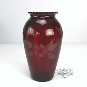 May include: A ruby red glass vase with a flared rim and etched floral design. The vase has a rounded body and a slightly tapered base. The etched design features stylized leaves and flowers. The vase is approximately 8 inches tall.