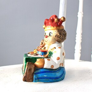 May include: A ceramic clown figurine playing a drum with a red and white polka dot hat and blue trousers.