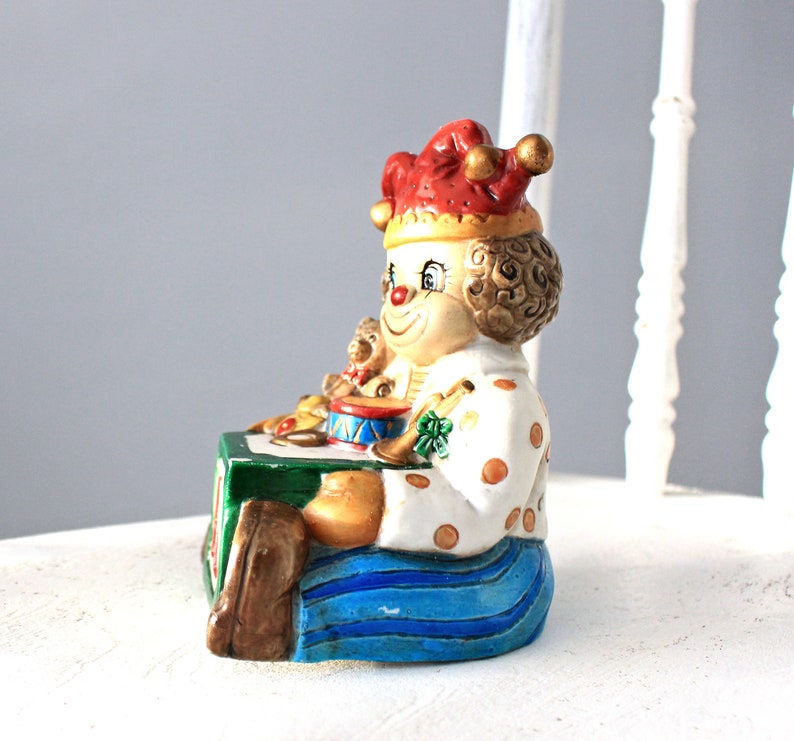 May include: A ceramic clown figurine playing a drum with a red and white polka dot hat and blue trousers.