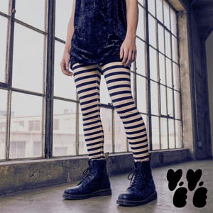 May include: Leggings featuring a horizontal striped pattern in black and beige. The leggings are paired with a black velvet-textured top and black lace-up leather boots. The design includes a repeating pattern of thin dark stripes on a light base.