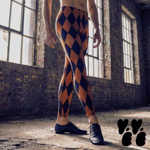 Puede incluir: Leggings con un patrón de diamantes repetido en tonos alternos de negro y naranja quemado. La prenda ajustada llega hasta los tobillos y se combina con zapatos negros con cordones. El texto Studio VéYé es visible en la tela.