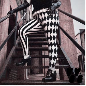 May include: Leggings featuring a black and white harlequin diamond pattern on the front and vertical black and white stripes on the side. The garment is paired with black leather gloves and black platform shoes with a decorative buckle detail.