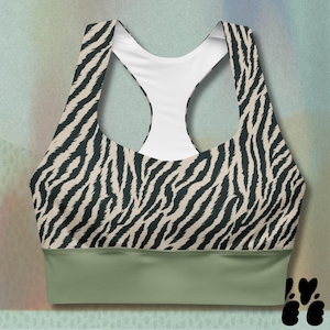May include: A sports bra featuring a zebra stripe design in black and beige. The bra has a racerback style with a white interior and a sage green band at the base. The design is sporty and fashionable.