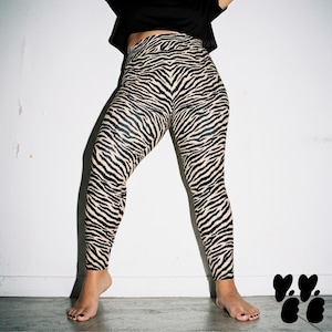 May include: High-waisted leggings featuring a black and beige zebra stripe pattern. The leggings have a fitted silhouette that extends to the ankles, showcasing a continuous animal print design across the entire fabric surface from waist to hem.
