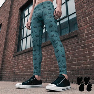 Peut inclure: Legging bleu sarcelle avec un motif répétitif de crânes et d'hélicoptères gris foncé. Le legging a une coupe ajustée et est porté avec des baskets basses en toile noire à semelles et lacets blancs. Le texte Studio YeYe est visible sur le tissu.