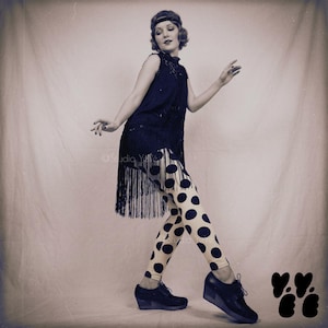 May include: A vintage-toned image of a woman in a flapper-style outfit. She wears a black fringed dress over cream-colored leggings with large black polka dots. Black wedge shoes and a headband complete the look. The image has a sepia tone.