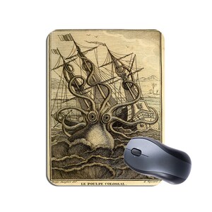 May include: A rectangular mouse mat with a vintage black and white illustration of a giant octopus attacking a sailing ship. The text "LE POULPE COLOSSAL" is at the bottom. A grey wireless mouse is next to the mouse mat.