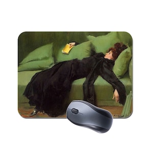 May include: A woman in a black dress lies on a green sofa with a yellow book in her hand. The sofa has cushions and is in a room with green walls.