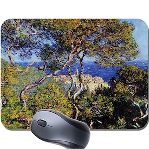 May include: A mouse mat featuring a painting of a lush green landscape with a town in the distance. The painting is in a vibrant style with blue skies and a bright green tree in the foreground.