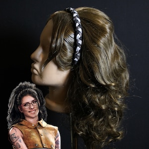 May include: A brown wig with long, curly hair. The wig is styled with a black and white braided headband.