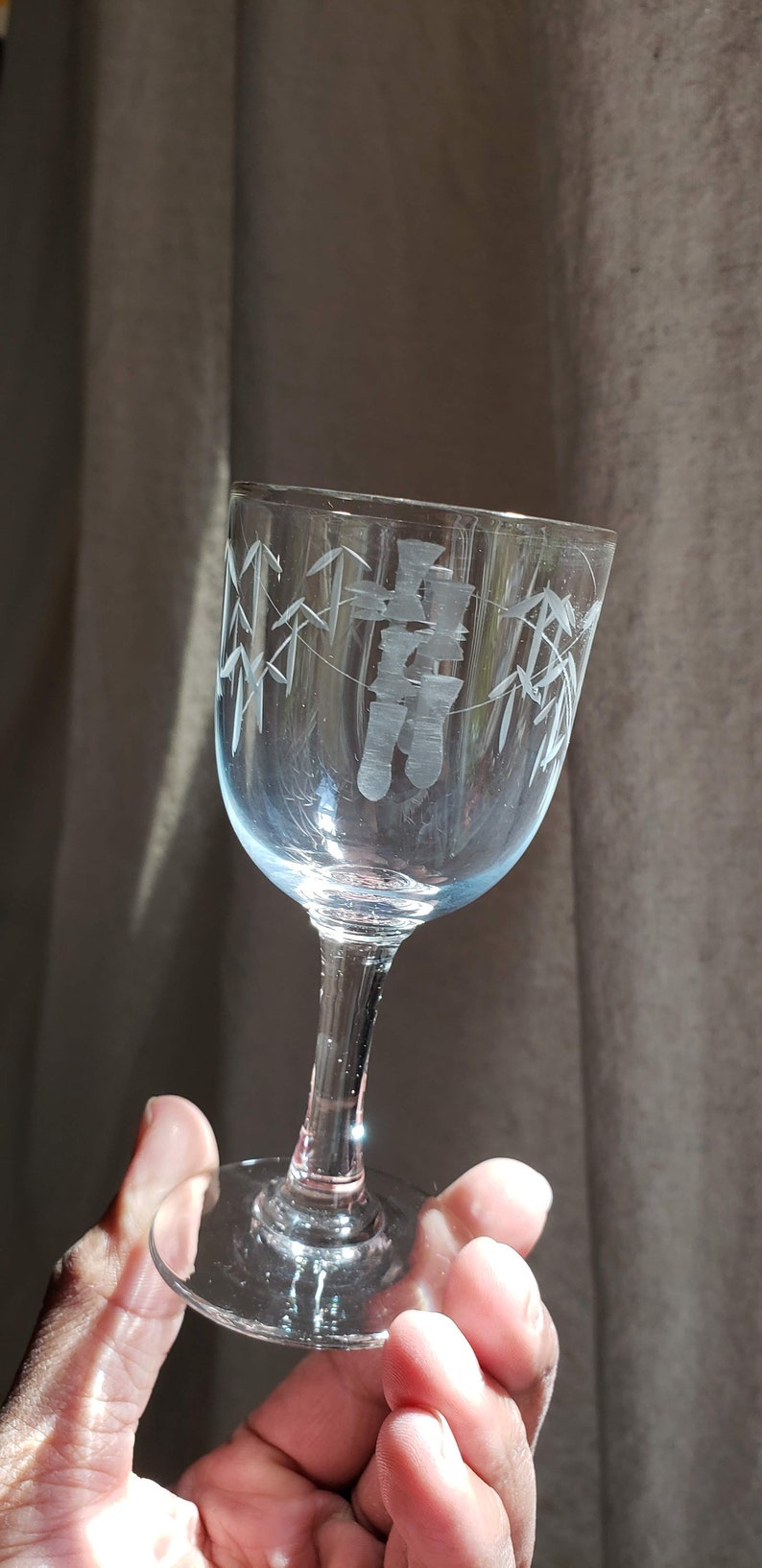 May include: A clear glass wine glass with an etched design of bamboo and Chinese characters. The glass has a short stem and a round base.