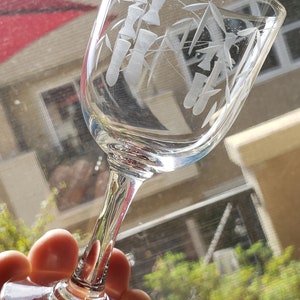 May include: A clear glass wine glass with an etched design of bamboo stalks. The glass is held in a hand.