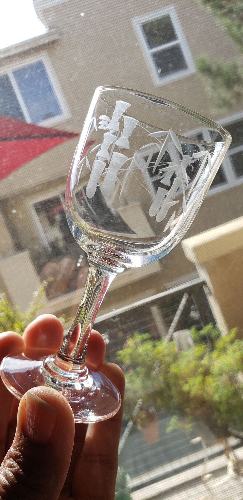 May include: A clear glass wine glass with an etched design of bamboo stalks. The glass is held in a hand.